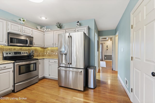 kitchen with appliances with stainless steel finishes, light wood-style floors, light stone counters, and tasteful backsplash