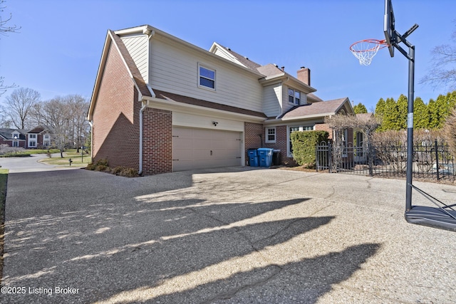 rear view of property with a garage, brick siding, fence, driveway, and a chimney