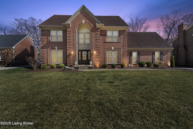 view of front of home featuring brick siding, a front yard, and a shingled roof