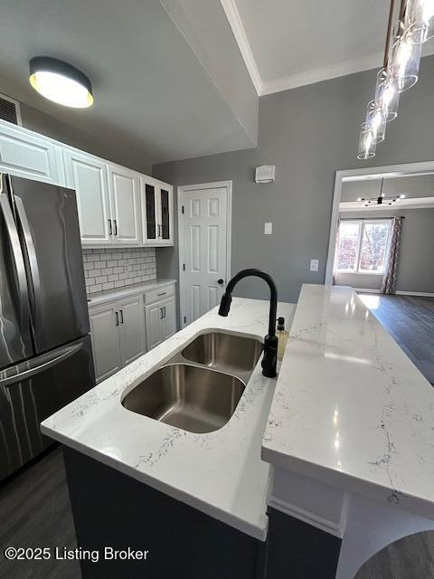 kitchen featuring ornamental molding, freestanding refrigerator, white cabinetry, a sink, and an island with sink