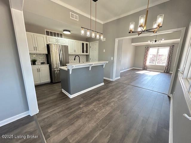 kitchen featuring visible vents, ornamental molding, dark wood-style floors, freestanding refrigerator, and decorative backsplash