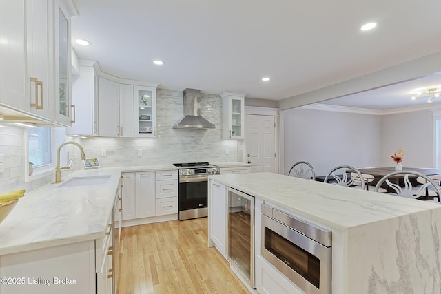 kitchen featuring beverage cooler, a sink, appliances with stainless steel finishes, light stone countertops, and wall chimney exhaust hood