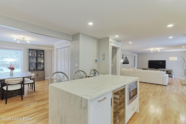 kitchen with wine cooler, stainless steel microwave, light wood-type flooring, and white cabinetry