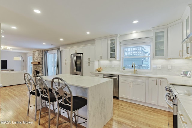 kitchen with stainless steel appliances, a fireplace, a sink, open floor plan, and a kitchen bar