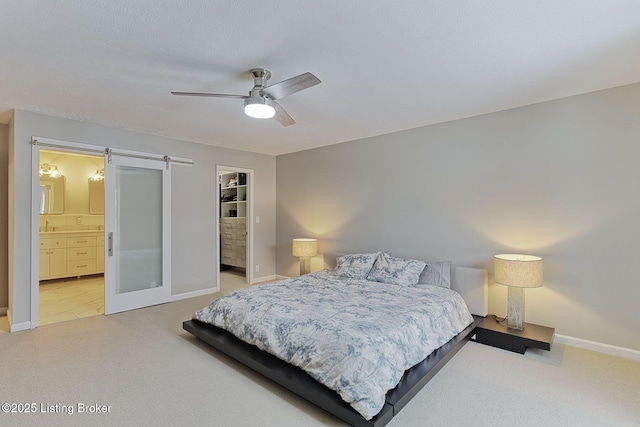 bedroom with light carpet, a barn door, baseboards, ceiling fan, and a walk in closet