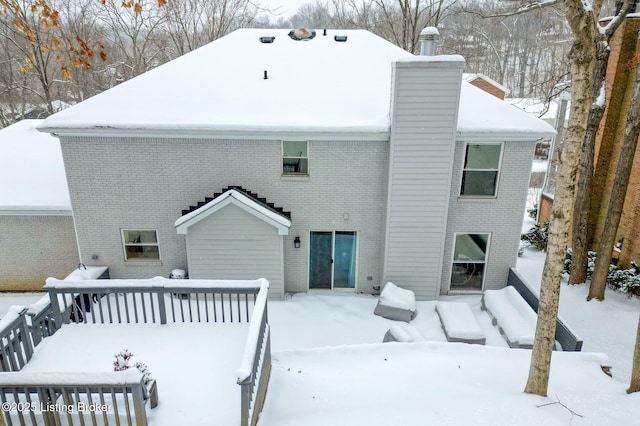 snow covered back of property featuring a chimney, a deck, and brick siding