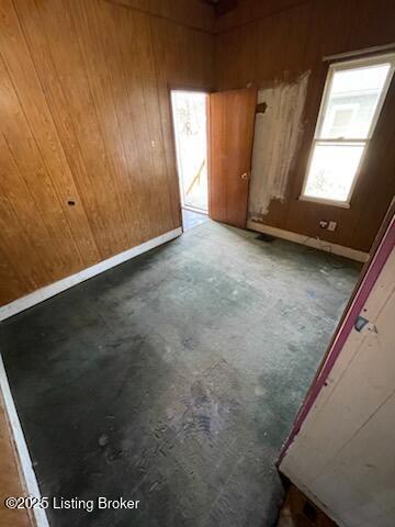 unfurnished room featuring concrete flooring, wood walls, and baseboards