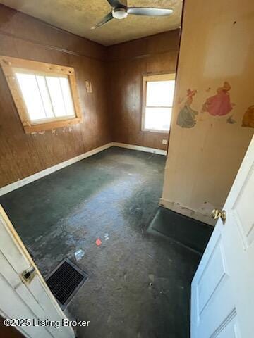 unfurnished room with baseboards, visible vents, a ceiling fan, concrete flooring, and wood walls