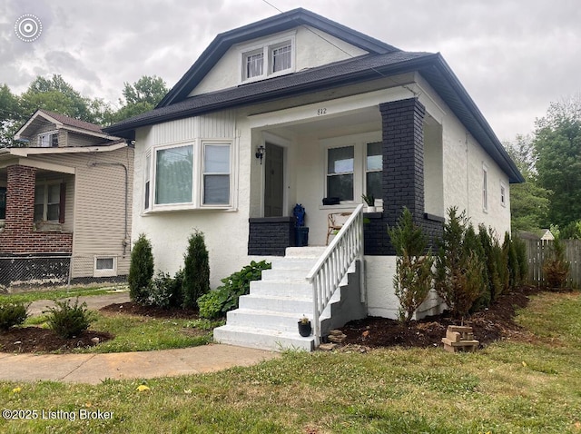 bungalow-style home with brick siding, a front yard, a porch, and stucco siding