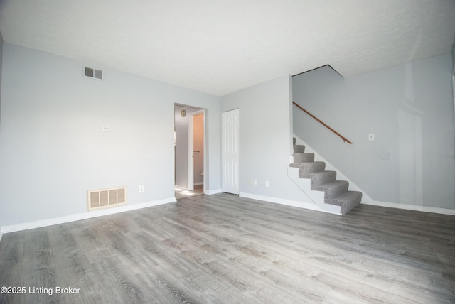 unfurnished room featuring stairs, wood finished floors, visible vents, and baseboards