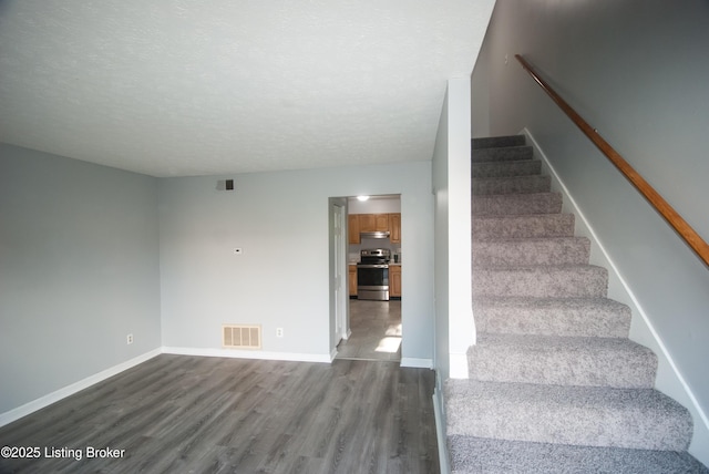 staircase featuring visible vents, a textured ceiling, baseboards, and wood finished floors