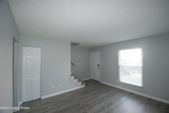 unfurnished room featuring wood finished floors, a textured ceiling, baseboards, and stairs