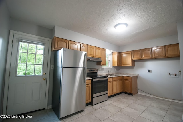 kitchen featuring appliances with stainless steel finishes, light countertops, a textured ceiling, under cabinet range hood, and a sink