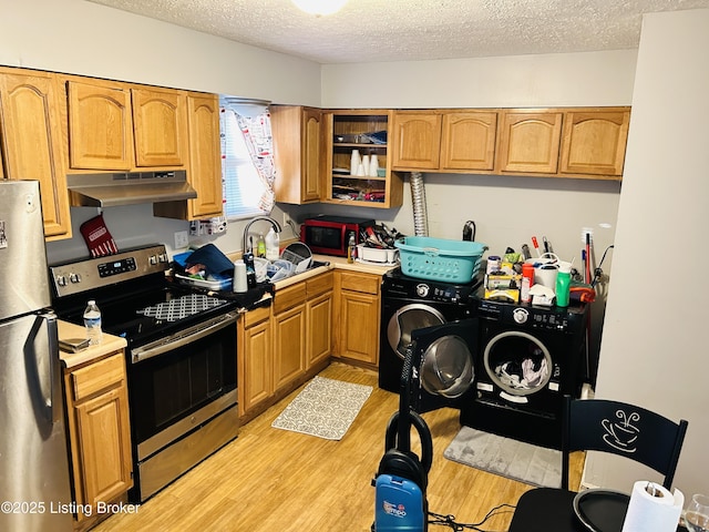 kitchen with under cabinet range hood, stainless steel appliances, a sink, independent washer and dryer, and light wood finished floors