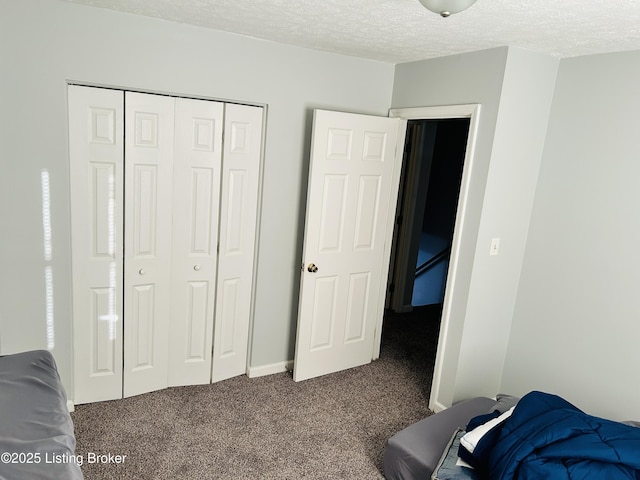 bedroom with a textured ceiling, dark colored carpet, and a closet