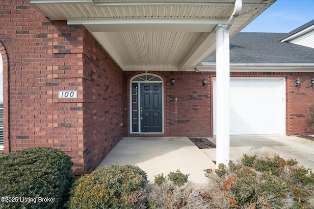 entrance to property featuring a garage, driveway, a shingled roof, and brick siding