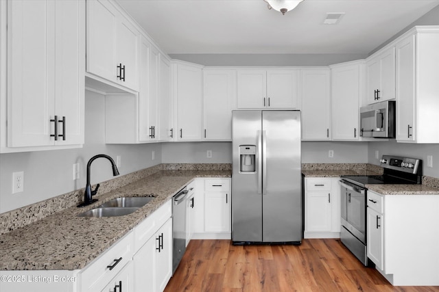 kitchen with visible vents, appliances with stainless steel finishes, light stone counters, white cabinetry, and a sink