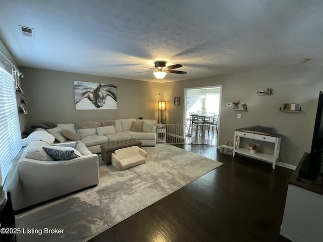 living room featuring dark wood-style floors, visible vents, ceiling fan, and a textured ceiling