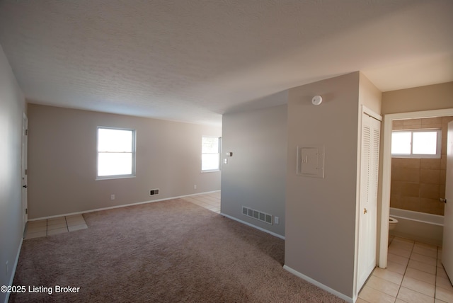 empty room with light carpet, baseboards, visible vents, a textured ceiling, and light tile patterned flooring