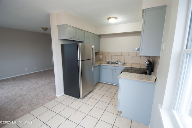 kitchen featuring light countertops, light colored carpet, stove, freestanding refrigerator, and a sink