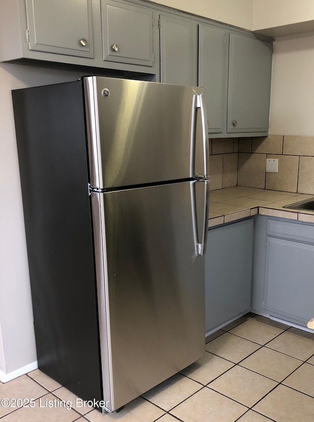 kitchen featuring light tile patterned floors, gray cabinets, tile counters, freestanding refrigerator, and decorative backsplash