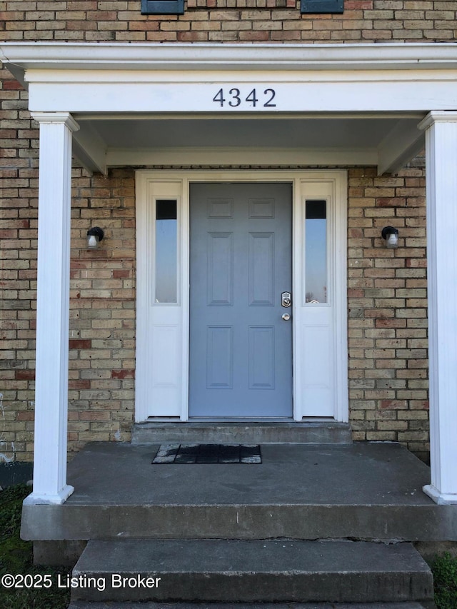 view of exterior entry with a shingled roof and brick siding