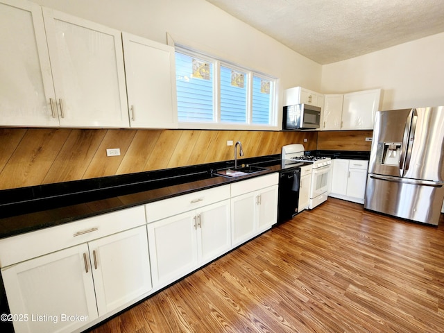 kitchen featuring stainless steel appliances, dark countertops, a sink, and white cabinetry