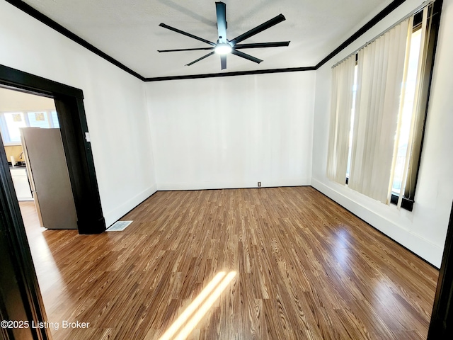 spare room featuring baseboards, visible vents, a ceiling fan, ornamental molding, and wood finished floors