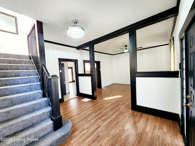 foyer with ornamental molding, ceiling fan, wood finished floors, baseboards, and stairs