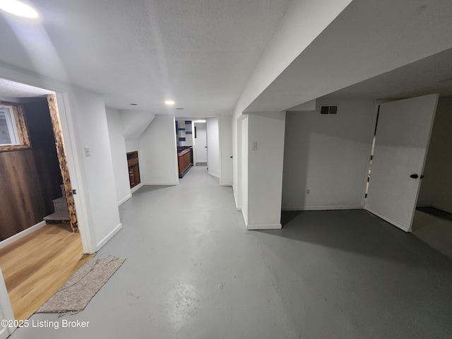 finished below grade area featuring visible vents, a textured ceiling, and baseboards