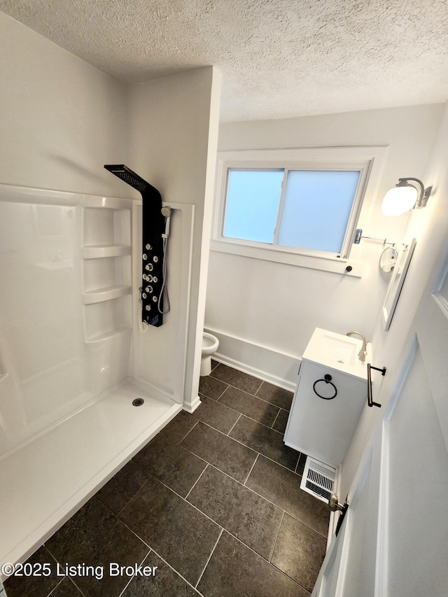 bathroom featuring a textured ceiling, visible vents, vanity, baseboards, and walk in shower