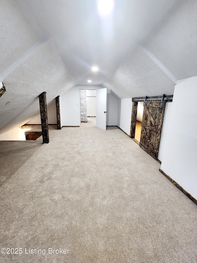 bonus room featuring a barn door, baseboards, lofted ceiling, a textured ceiling, and carpet floors