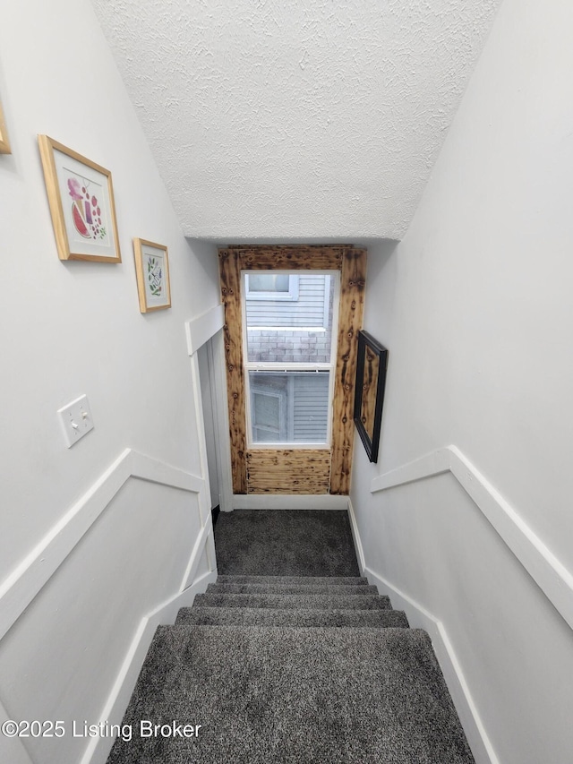 stairway with a textured ceiling, carpet, and baseboards