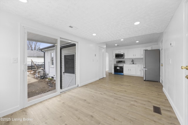 unfurnished living room featuring light wood-type flooring, a textured ceiling, visible vents, and a sink