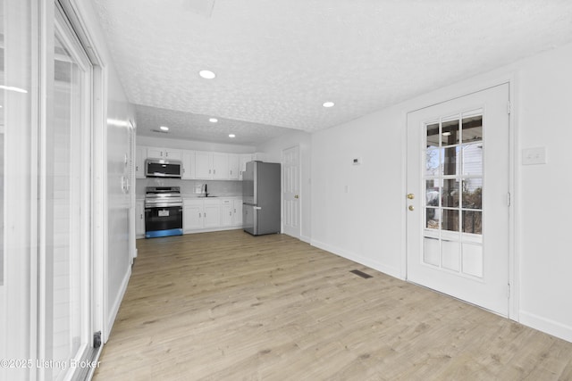 kitchen featuring light countertops, light wood-style flooring, appliances with stainless steel finishes, white cabinets, and a textured ceiling