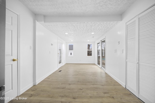 hallway featuring light wood-type flooring, a textured ceiling, baseboards, and recessed lighting