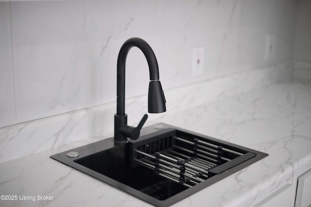 room details featuring light stone counters, decorative backsplash, and a sink