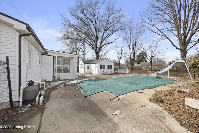 view of swimming pool featuring a covered pool, an outbuilding, fence, a water slide, and a patio area