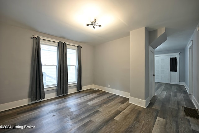 spare room with dark wood-type flooring, visible vents, and baseboards