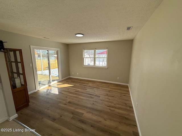 unfurnished room with visible vents, a textured ceiling, baseboards, and wood finished floors