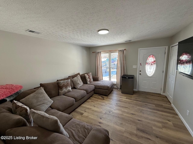 living room with baseboards, a textured ceiling, visible vents, and wood finished floors