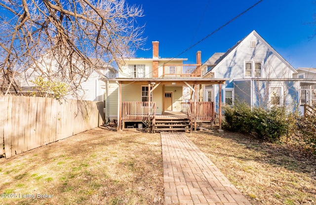 back of property featuring a balcony, a chimney, fence, and a lawn