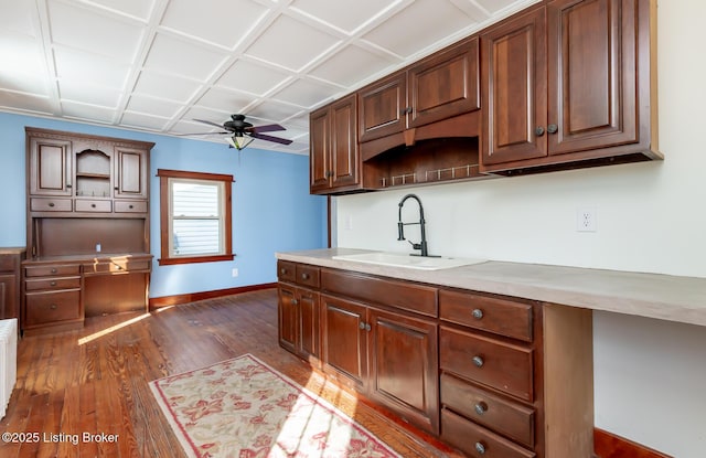 kitchen with baseboards, a ceiling fan, dark wood-style flooring, light countertops, and a sink