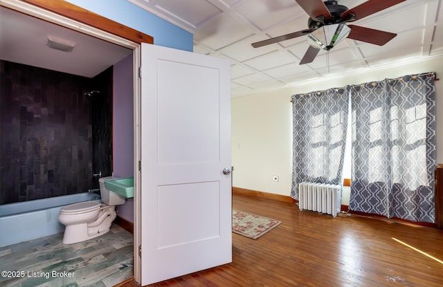 bathroom featuring radiator, wood-type flooring, shower / bathing tub combination, toilet, and baseboards