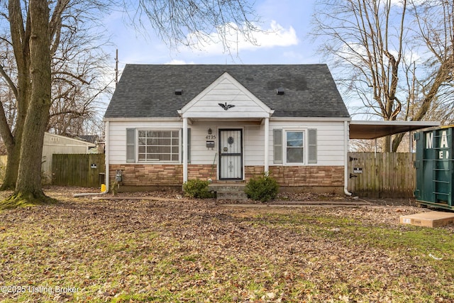 view of front of property featuring stone siding, an attached carport, a shingled roof, and fence