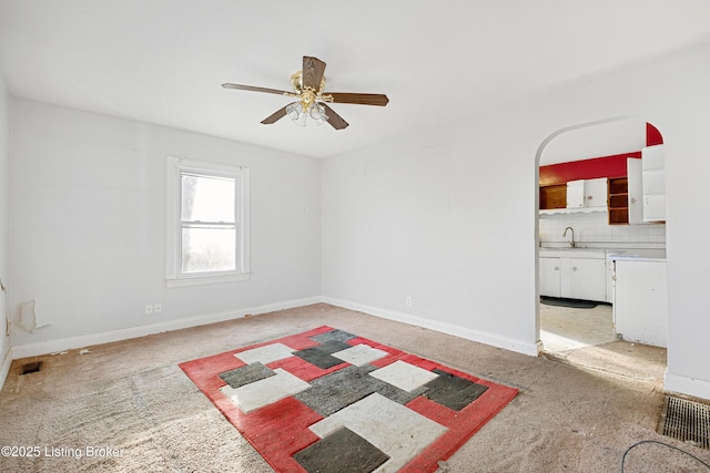 interior space featuring baseboards, arched walkways, a ceiling fan, light colored carpet, and a sink