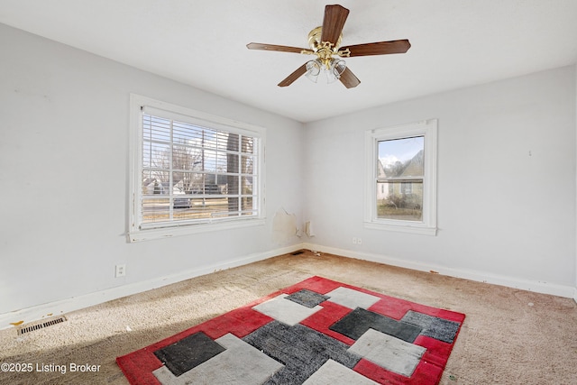 spare room featuring carpet floors, a ceiling fan, visible vents, and baseboards