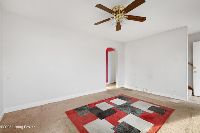 spare room with carpet, baseboards, arched walkways, and ceiling fan