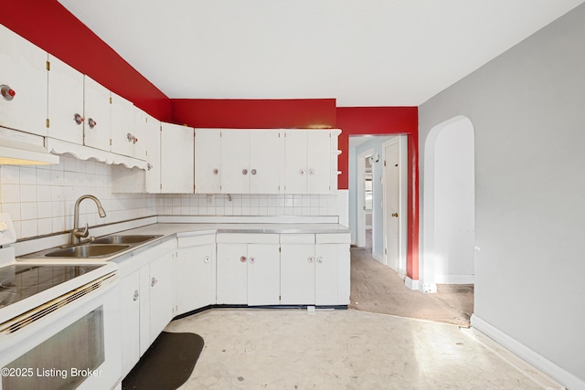 kitchen with tasteful backsplash, arched walkways, white cabinets, and white range with electric cooktop