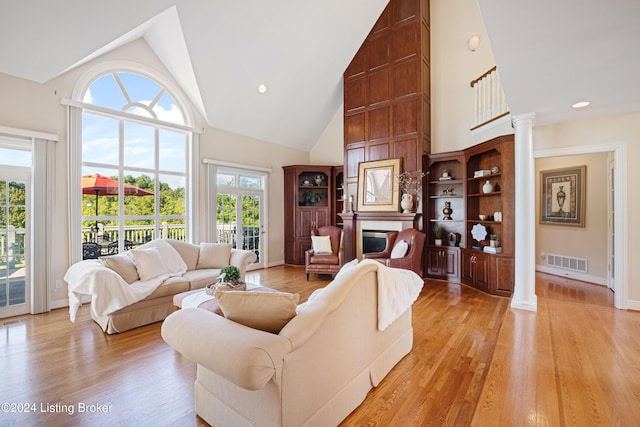 living area featuring high vaulted ceiling, a fireplace, visible vents, light wood-type flooring, and decorative columns